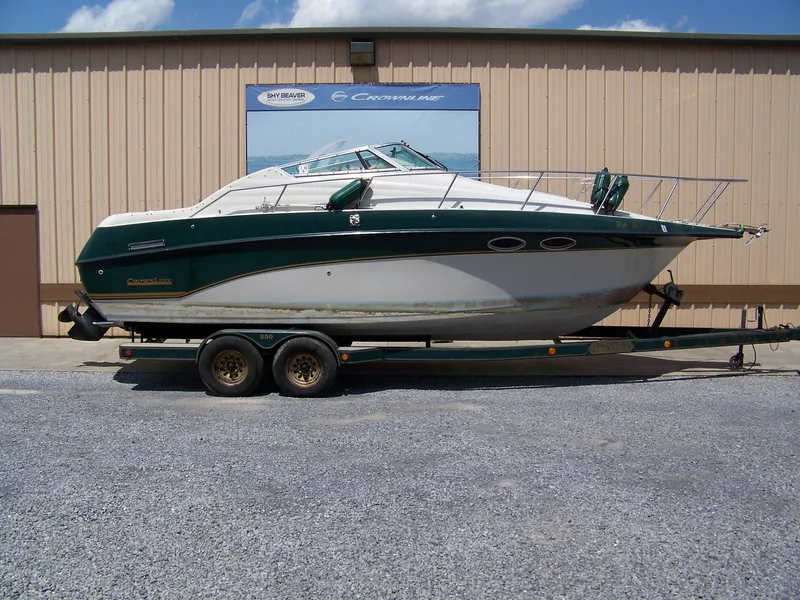 The Image of 1996 Crownline 250 CR boat on trailer, parked outside a beige building under a blue sky. - 1