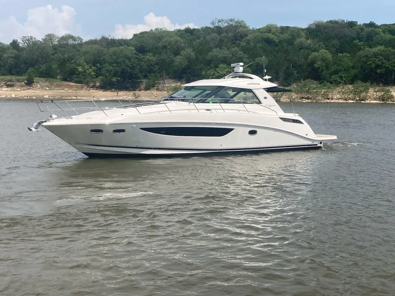 The Image of 2015 Sea Ray 450 Sundancer yacht cruising on a calm lake with forested shoreline. - 1