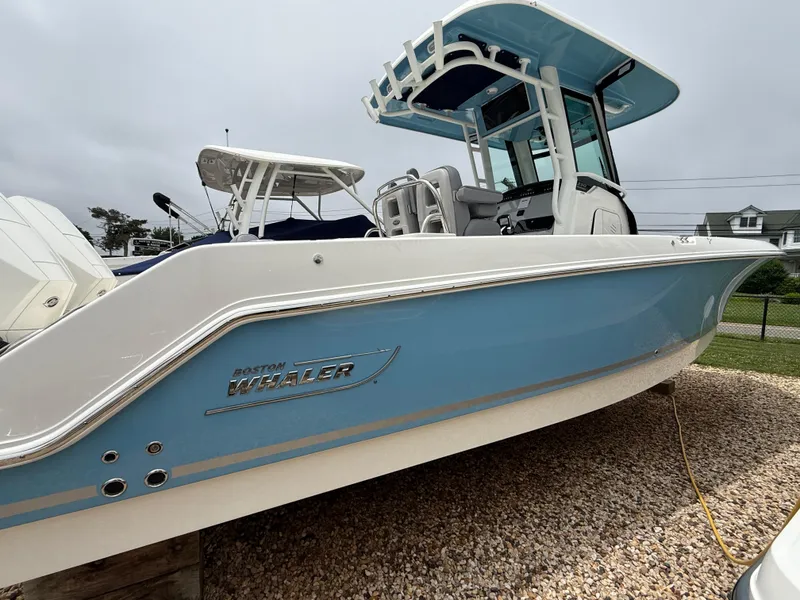 Slide: The Image of 2026 Boston Whaler 250 Outrage boat with blue hull, parked on gravel. - 2