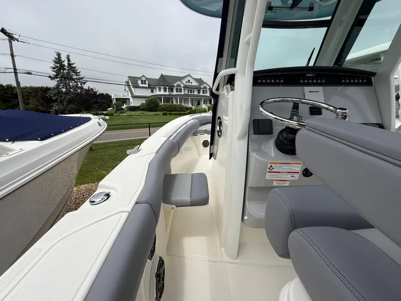 Slide: The Image of 2026 Boston Whaler 250 Outrage boat interior with steering wheel and seating, near a house. - 25
