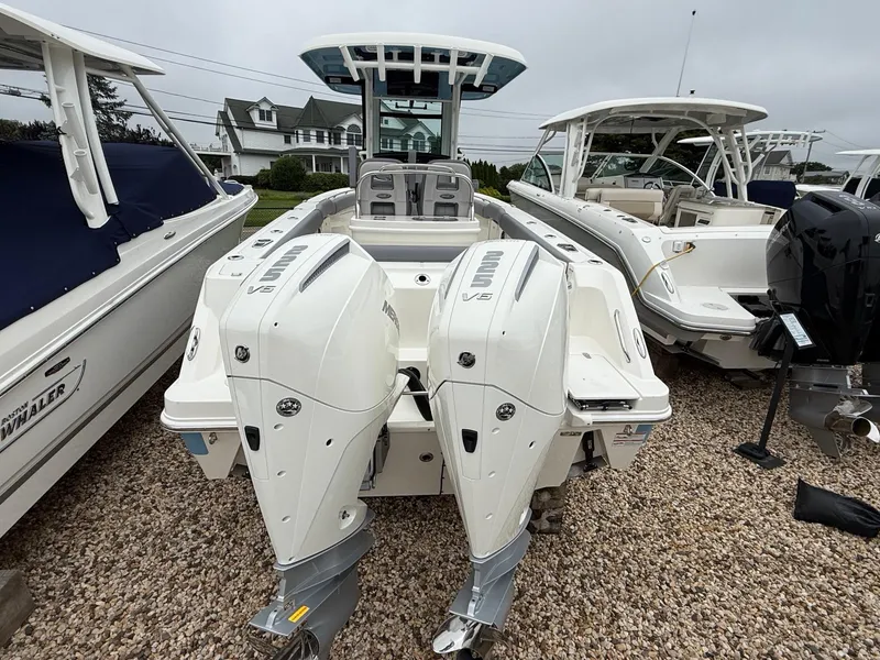 Slide: The Image of 2026 Boston Whaler 250 Outrage with dual outboard engines, displayed on gravel lot. - 6