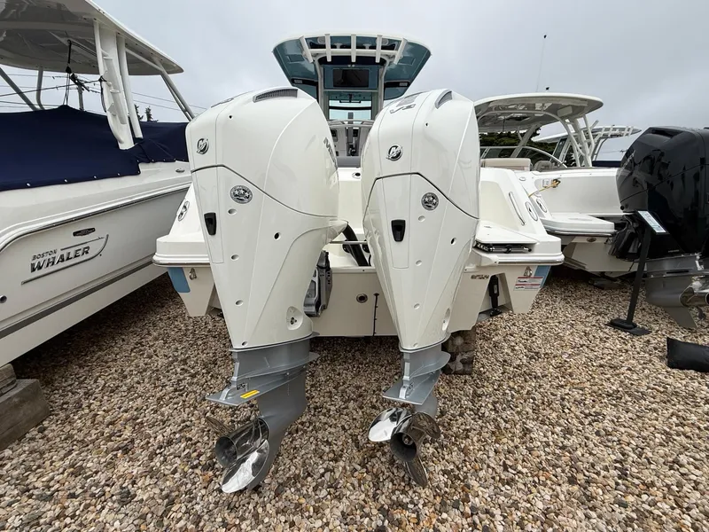 Slide: The Image of 2026 Boston Whaler 250 Outrage with dual outboard engines on gravel lot. - 7