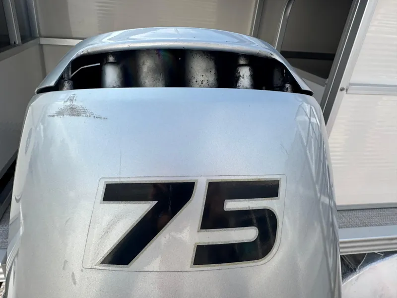 Slide: The Image of Silver outboard motor with "75" marking, attached to a 2006 Manitou 24 Legacy boat. - 13