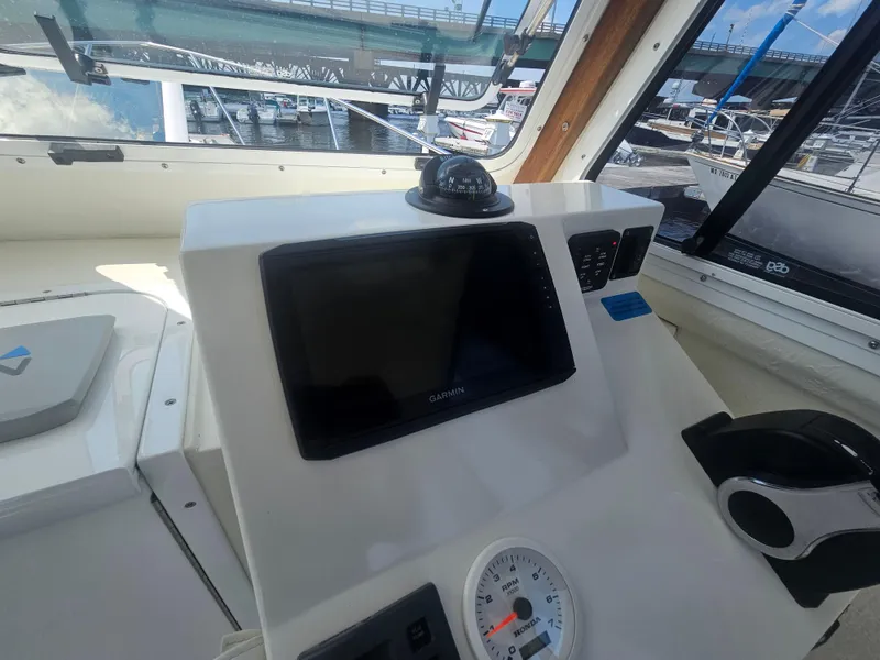 Slide: The Image of 2019 Eastern 248 Explorer boat dashboard with Garmin display and compass, docked near a bridge. - 30