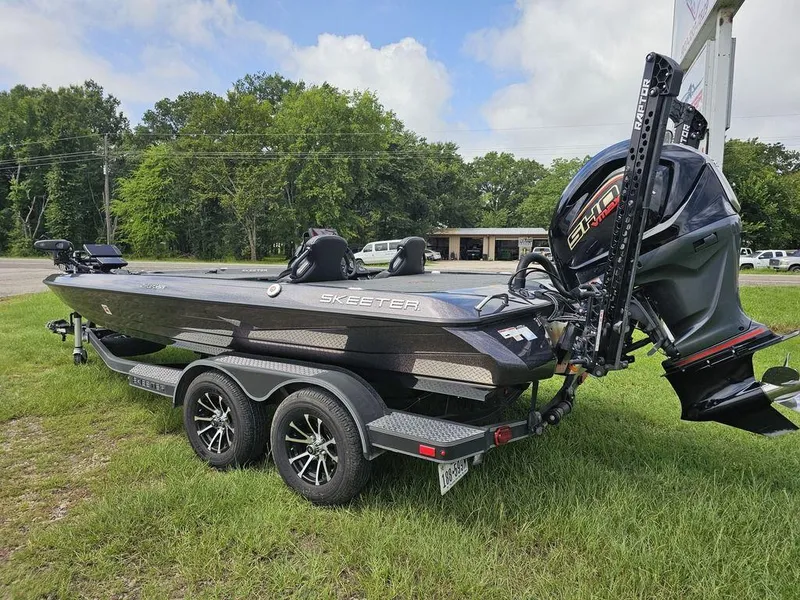 Slide: The Image of 2023 Skeeter ZXR 20 bass boat on trailer, parked on grass, with trees in background. - 9