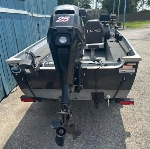 Slide: The Image of 2013 Lund 1400 Fury SS boat with outboard motor, parked near a blue building. - 3
