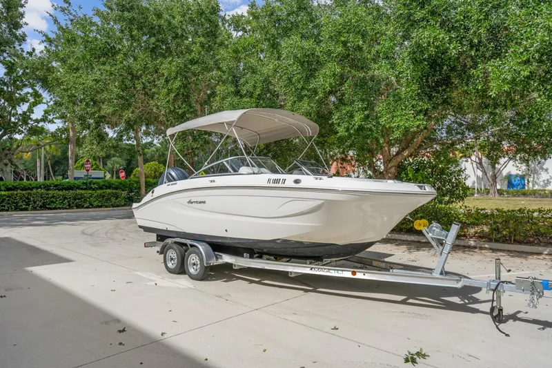 Slide: The Image of 2025 Hurricane SunDeck 2050 OB boat on trailer, parked outdoors with trees in the background. - 5