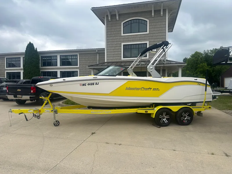 The Image of 2018 MasterCraft NXT22 boat on yellow trailer, parked outside a building. - 0