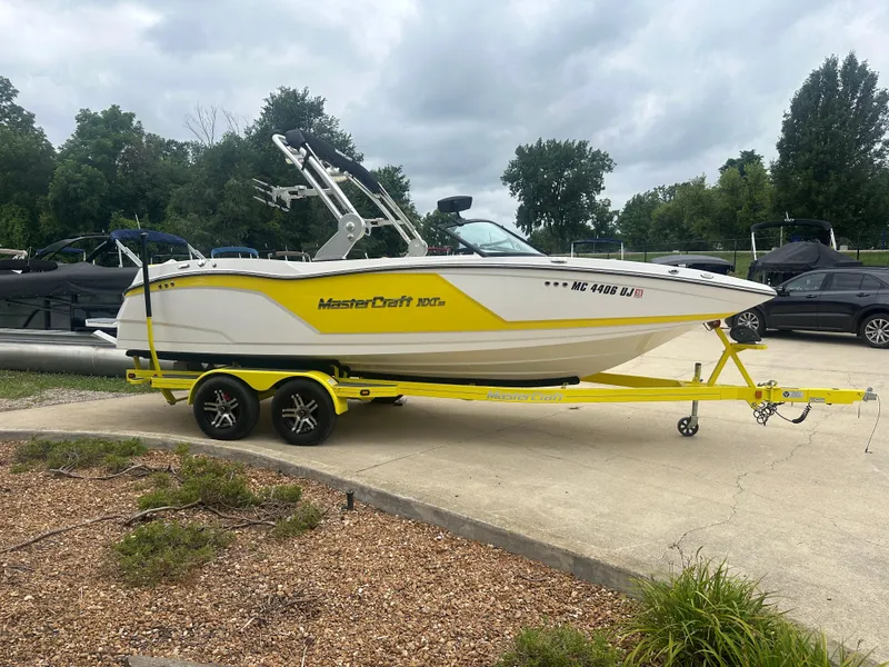 Slide: The Image of 2018 MasterCraft NXT22 boat on yellow trailer, parked outdoors on a cloudy day. - 23