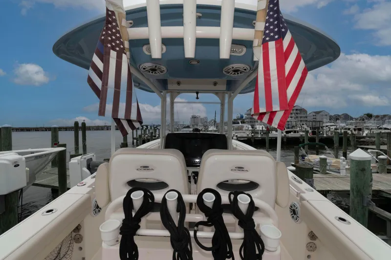 Slide: The Image of 2023 Cobia 280 Center Console boat docked with American flags, marina background. - 21