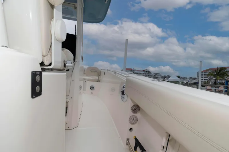 Slide: The Image of 2023 Cobia 280 Center Console boat interior with white seating and marina background. - 22