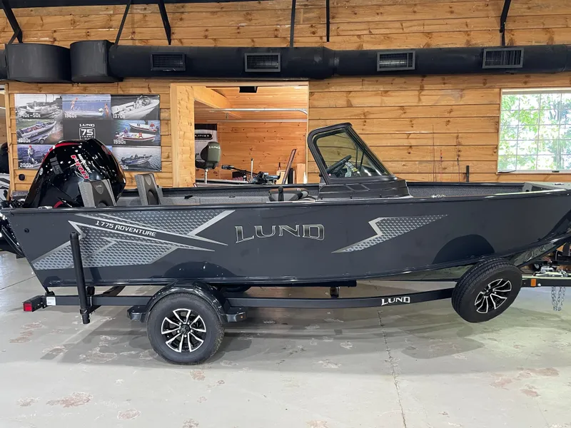 Slide: The Image of 2026 Lund 1775 Adventure Sport boat in showroom, side view, black exterior, on trailer. - 0