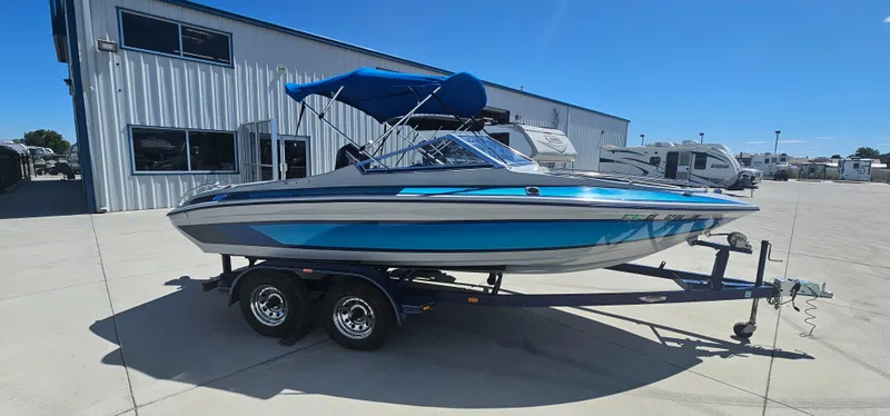 Slide: The Image of 1989 Galaxie 1900 Starion boat with blue canopy on trailer, parked outside a building. - 2
