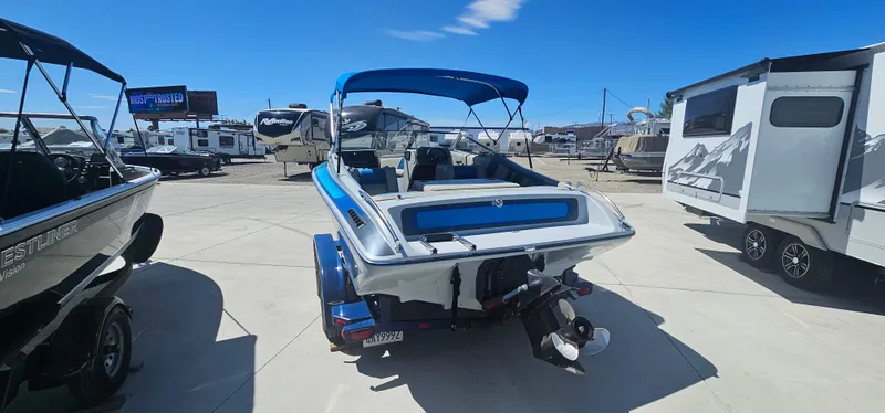 Slide: The Image of 1989 Galaxie 1900 Starion boat with blue canopy, parked near RVs and trailers. - 4
