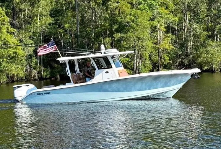 Slide: The Image of 2022 Sea Pro 320 DLX Offshore boat cruising on a serene lake with forest backdrop. - 1