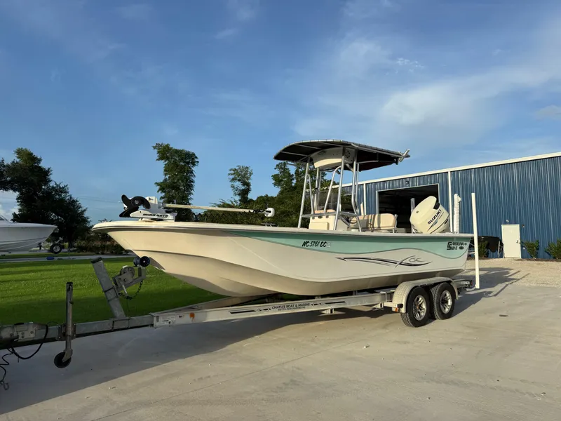 The Image of 2016 Carolina Skiff 238DLV boat on trailer, parked outdoors near blue building. - 1