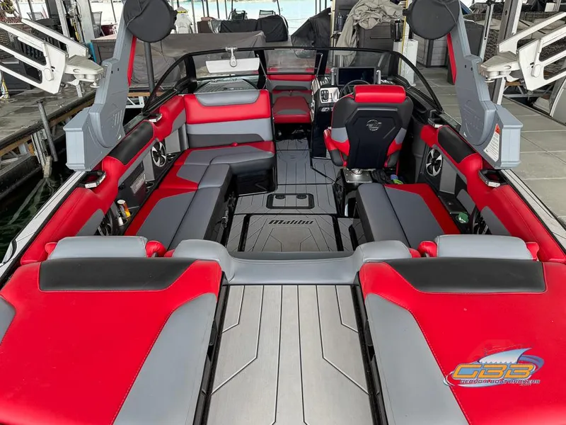 Slide: The Image of 2019 Malibu M235 boat interior with red and gray seating, docked at marina. - 16