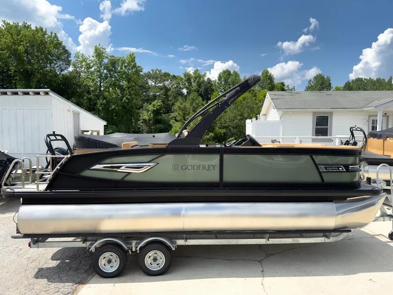 Slide: The Image of 2026 Godfrey AquaPatio 23' Flip Lounge Tritoon displayed indoors, featuring luxurious seating and powerful engine. - 2