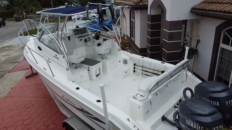 Slide: The Image of 2004 Cobia 250 Walk-Around boat with dual Yamaha engines, parked on a red driveway. - 17
