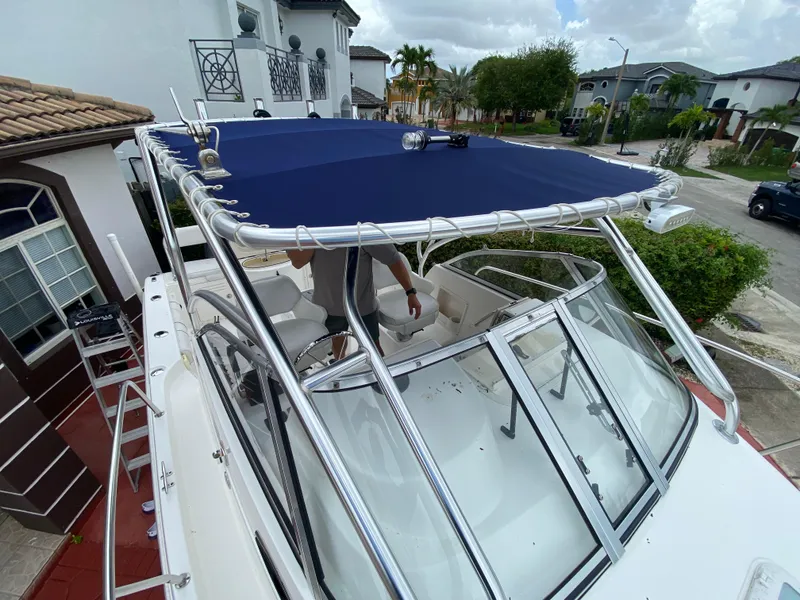 Slide: The Image of 2004 Cobia 250 Walk-Around boat with blue canopy, parked in residential area. - 18