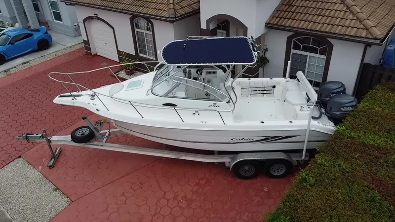 Slide: The Image of 2004 Cobia 250 Walk-Around boat on trailer in driveway, near a blue car. - 19