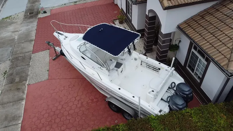 Slide: The Image of 2004 Cobia 250 Walk-Around boat with blue canopy parked on red brick driveway. - 21