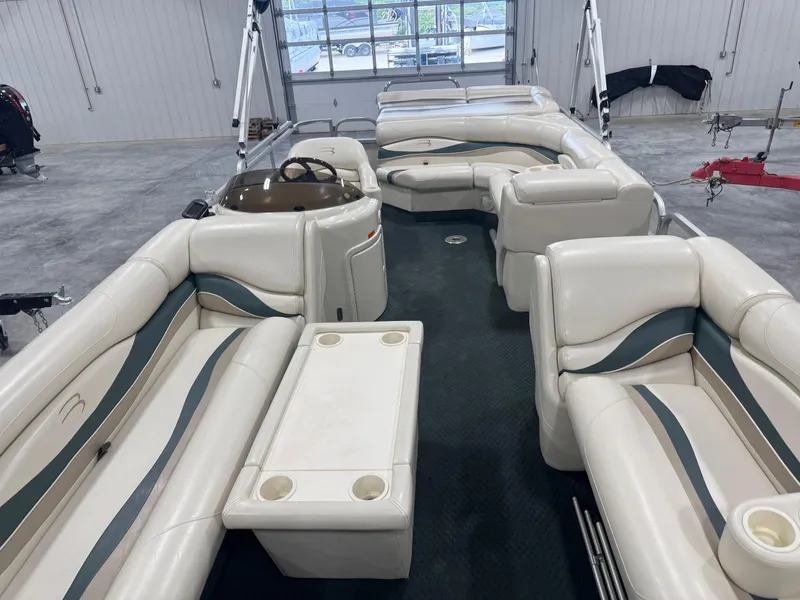 Slide: The Image of 2004 Bennington 2575 pontoon boat interior with beige seating and table in a garage. - 10