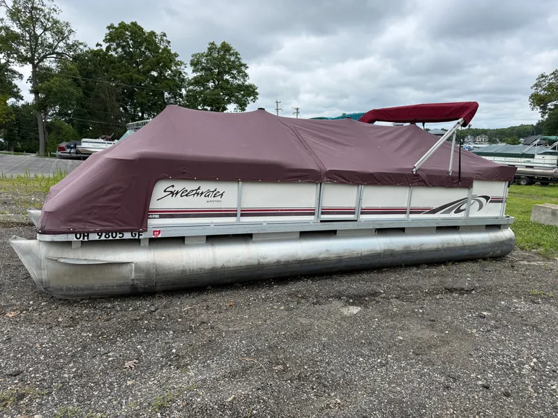 The Image of 1998 Sweetwater 24RE pontoon boat with maroon cover, parked on gravel. - 0