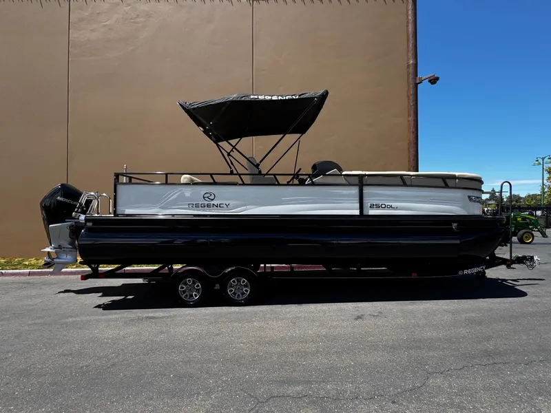 The Image of 2025 Regency 250 DL3 pontoon boat on trailer, parked outdoors under clear sky. - 0