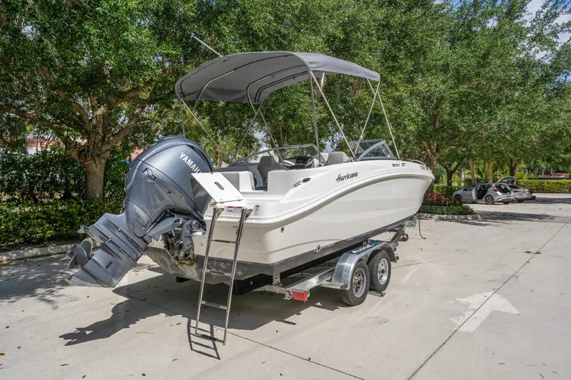 Slide: The Image of 2025 Hurricane SunDeck 217 OB boat on trailer, parked outdoors with trees in background. - 3