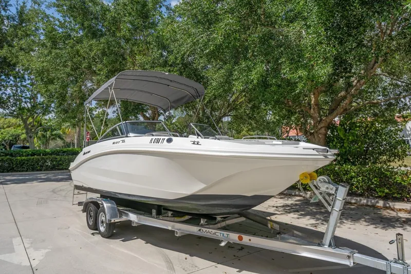 Slide: The Image of 2025 Hurricane SunDeck 217 OB boat on trailer, parked outdoors under trees. - 2