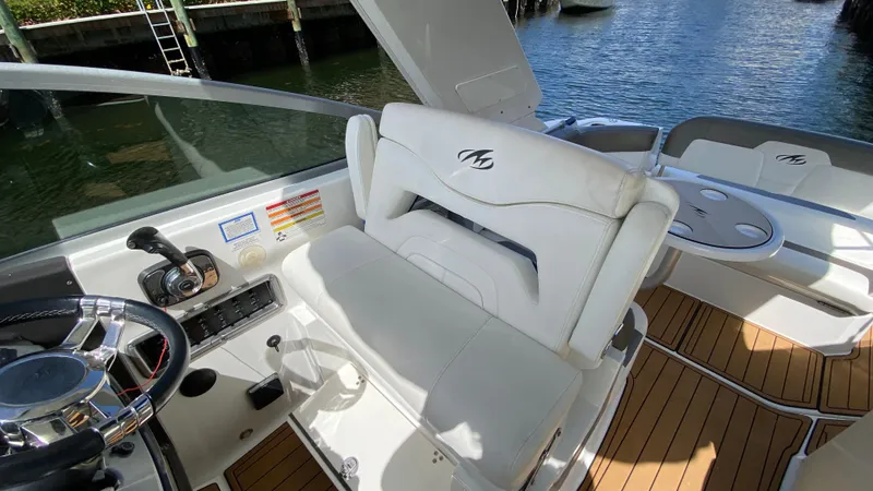 Slide: The Image of 2015 Monterey 295 Sport Yacht interior with steering wheel and seating, docked by water. - 10