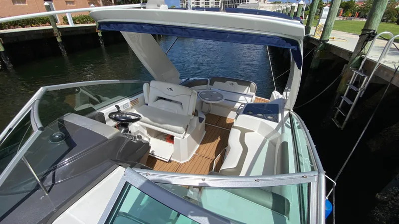 Slide: The Image of 2015 Monterey 295 Sport Yacht interior with helm, seating, and table, docked by water. - 13