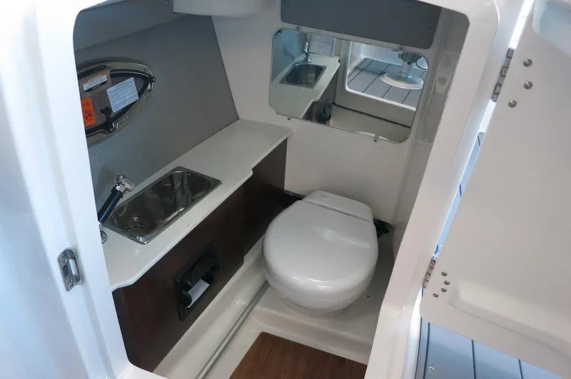 Slide: The Image of 2025 Chaparral 250 OSX boat interior with compact bathroom, featuring a toilet and sink. - 19