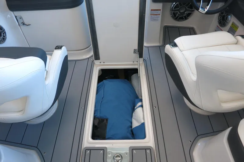 Slide: The Image of 2025 Chaparral 250 OSX boat interior with open storage compartment and white seating. - 23