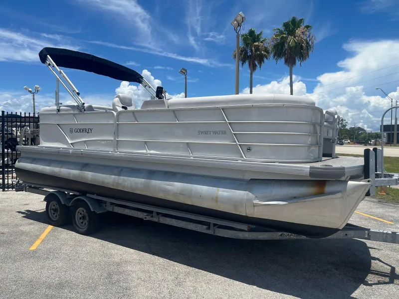 Slide: The Image of 2022 Godfrey SWEETWATER 2286 SFL pontoon boat on trailer, sunny day, palm trees. - 2
