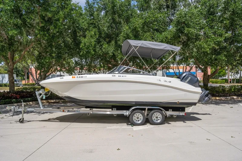Slide: The Image of 2025 Hurricane SunDeck 217 OB boat on trailer, parked outdoors with trees in background. - 4