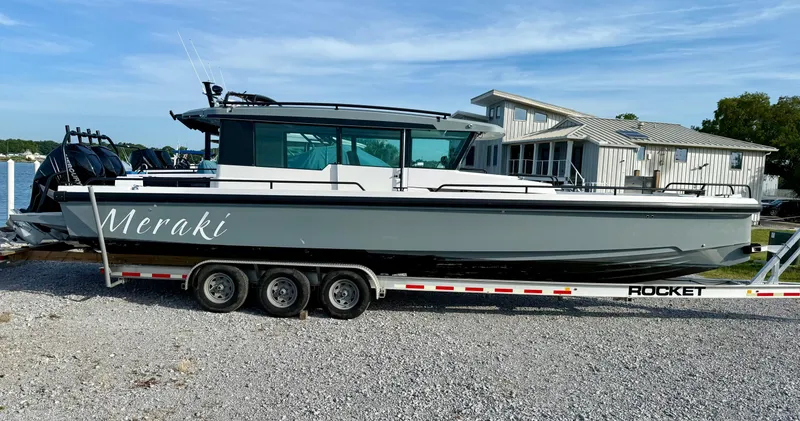 The Image of 2019 Axopar AX37XC boat named "Meraki" on a trailer by a lakeside house. - 1