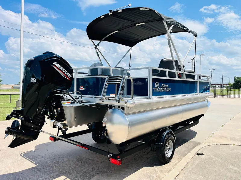 Slide: The Image of 2026 Sun Tracker Bass Buggy 18 DLX pontoon boat with Mercury outboard motor, parked outdoors. - 6