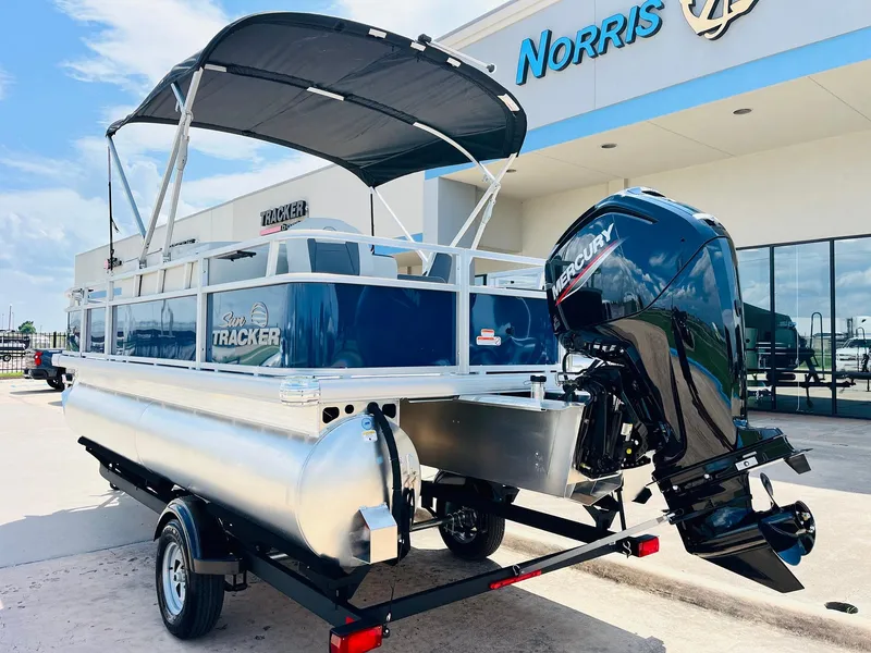 Slide: The Image of 2026 Sun Tracker Bass Buggy 18 DLX pontoon boat with Mercury engine, parked outside dealership. - 8