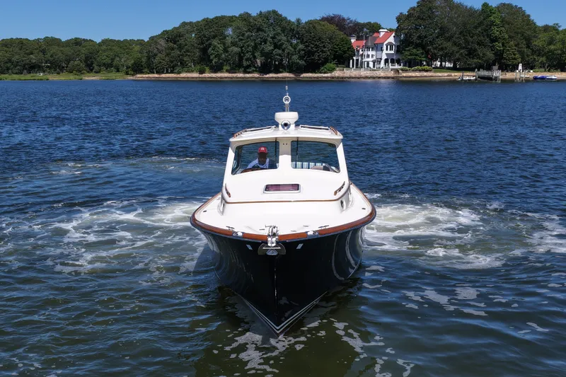 Slide: The Image of 2005 Hinckley 36 boat cruising on a serene lake with a scenic shoreline backdrop. - 15
