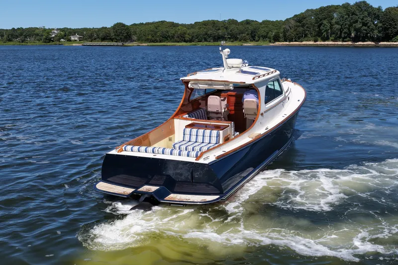 Slide: The Image of 2005 Hinckley 36 boat cruising on a serene lake with lush green shoreline. - 8