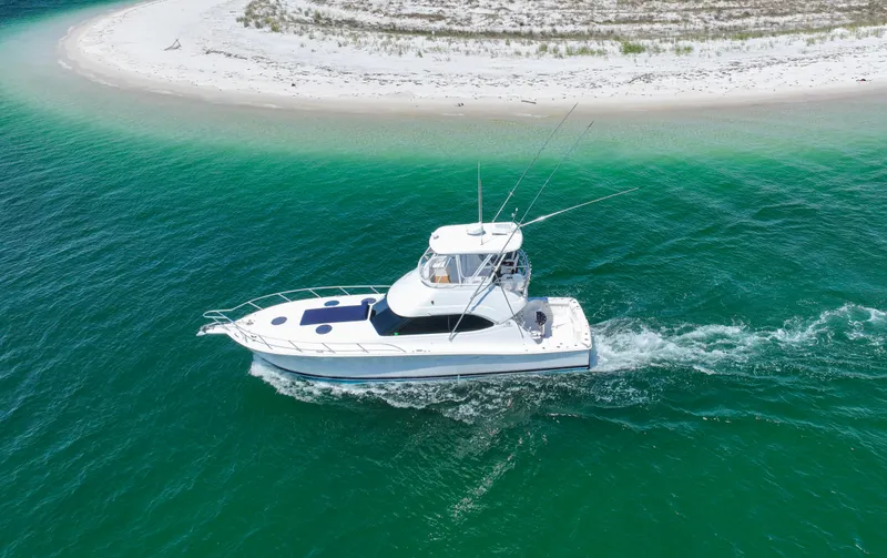 Slide: The Image of 2007 Riviera 42 Flybridge yacht cruising near a sandy beach in clear turquoise waters. - 12