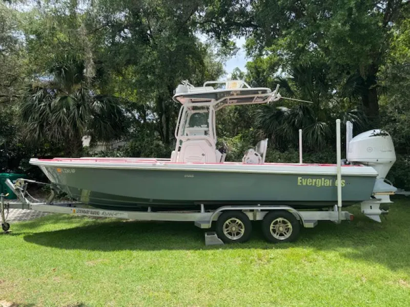 The Image of 2018 Everglades 243CC boat on trailer, parked on grass, surrounded by trees. - 0