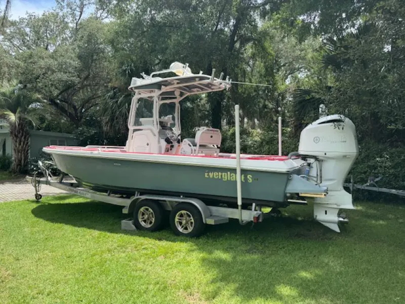 Slide: The Image of 2018 Everglades 243CC boat on trailer, parked on grass, surrounded by trees. - 1