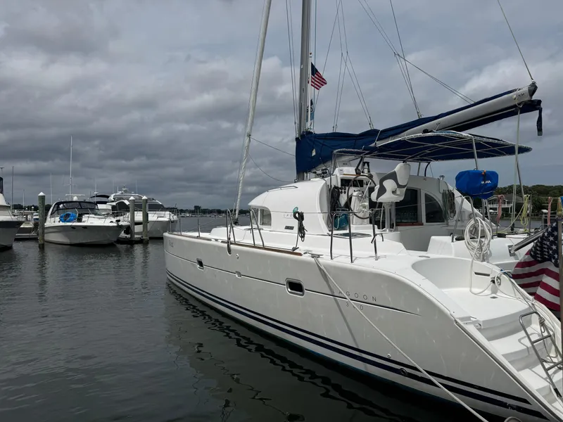 Slide: The Image of 2000 Lagoon 380 catamaran docked in a marina, with cloudy skies and nearby boats. - 3
