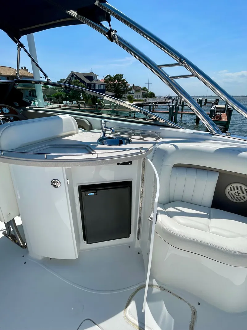 Slide: The Image of 2006 Cobalt 323 boat interior with seating, mini fridge, and sink, docked by waterfront homes. - 25