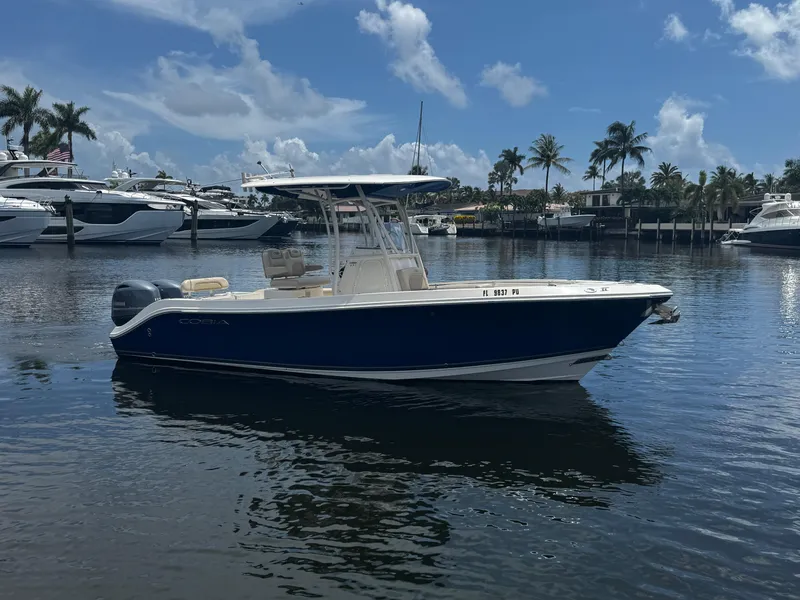 Slide: The Image of 2015 Cobia 237 Center Console boat on calm water, surrounded by palm trees and yachts. - 6