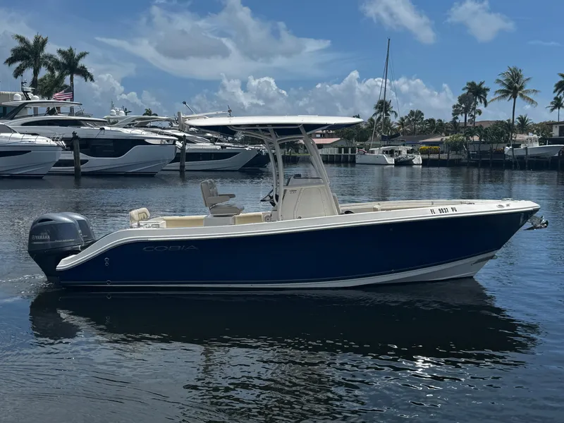 Slide: The Image of 2015 Cobia 237 Center Console boat on calm water, with palm trees and yachts in the background. - 7