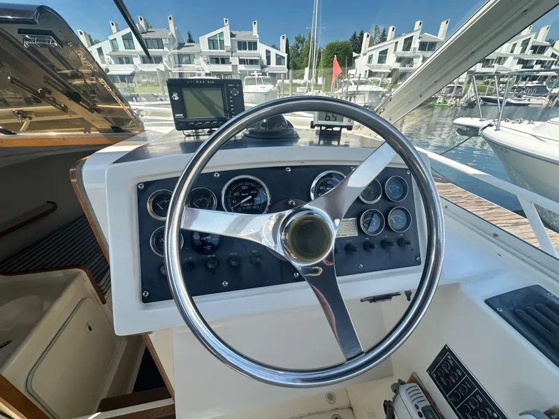 Slide: The Image of Cockpit of 1988 Bertram 28 Moppie boat with steering wheel and gauges, docked near modern buildings. - 12